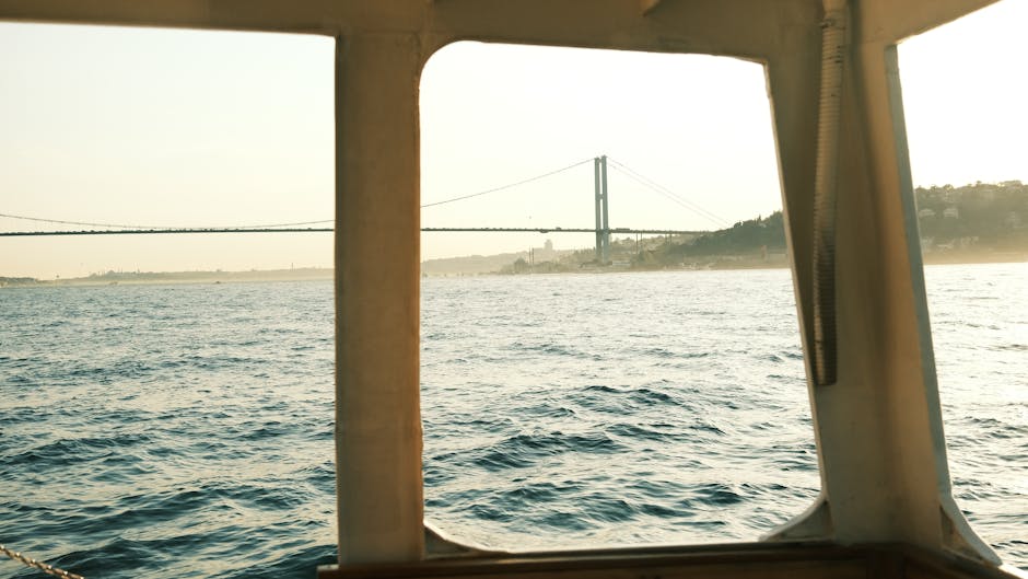 Scenic view from a boat of a suspension bridge at golden hour over calm waters.