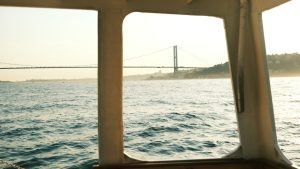 Scenic view from a boat of a suspension bridge at golden hour over calm waters.